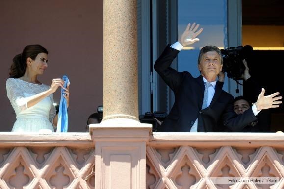 Mauricio se contonea. la Primera Dama observa y sostiene la banda presidencial.