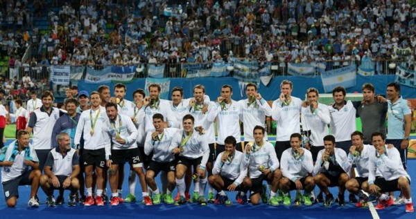 La foto soñada: el plantel y cuerpo técnico con el oro, y detrás la hinchada argentina.