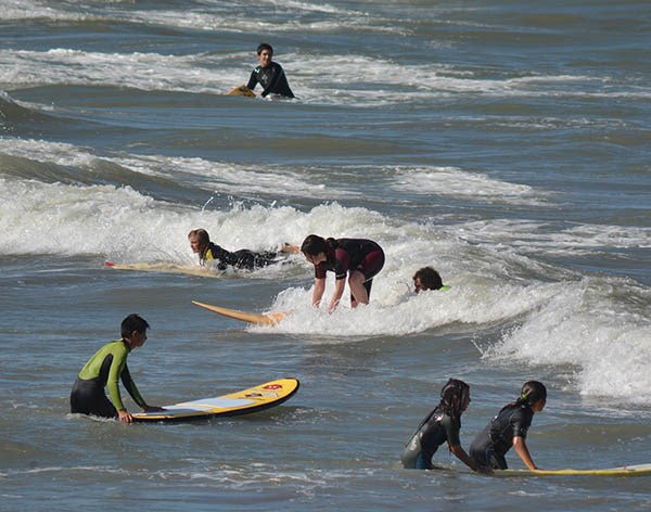 Chicos y chicas aprenden y se divierten en el agua con sus tablas de surf, en la Escuelita de Playa Unión.