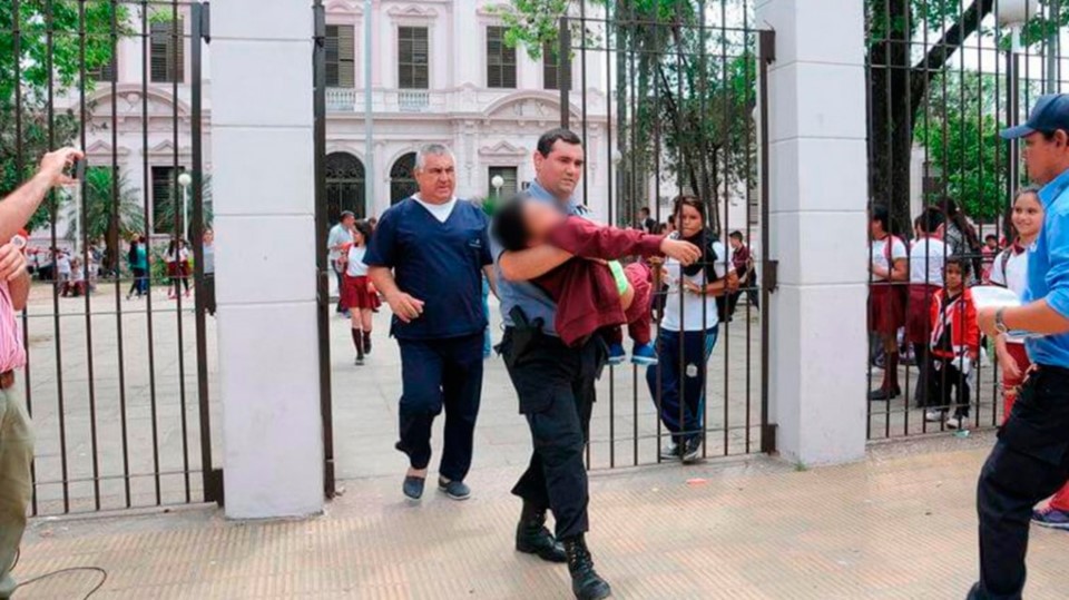 Un policía retira a uno de los alumnos que se desmayaron debido al potente veneno que se echó un día antes en la escuela.