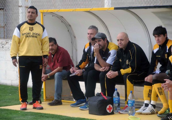 Víctor Zwenger toma nota en el banco de suplentes del Deportivo Madryn, acompañado por Edgar Galeano y el resto del cuerpo técnico.