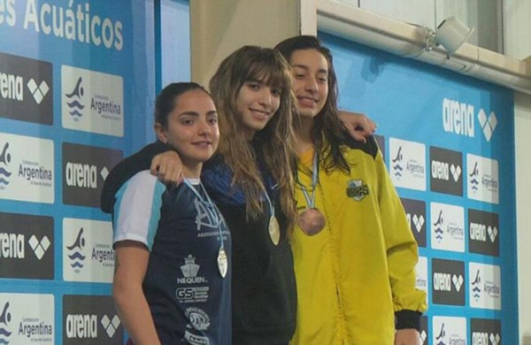 La nadadora capitalina Julieta Lema (centro), con su medalla de oro, abrazando a las chicas del podio.