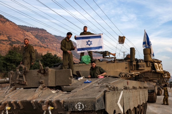 Un soldado israelí despliega una bandera mientras se encuentra en lo alto de la torreta de un carro de combate