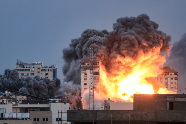 Personas paradas en una azotea observan cómo una bola de fuego y humo se eleva sobre un edificio en la ciudad de Gaza.