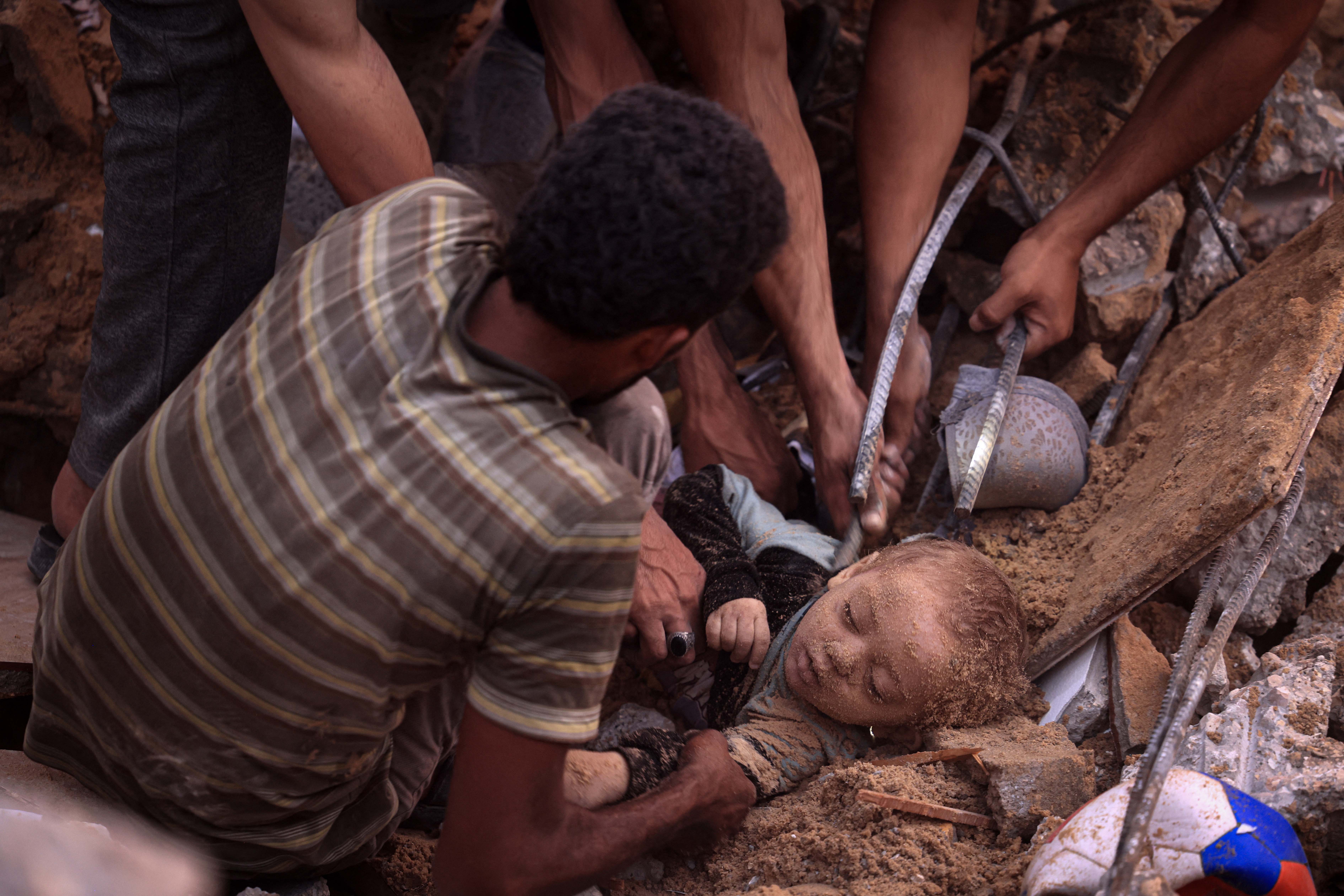 Palestinos desentierran el cadáver de un niño de entre los escombros de un edificio del campo de refugiados de Nuseirat.