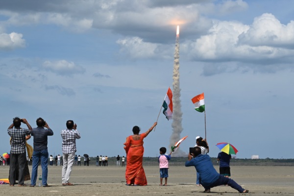 Varias personas ondean banderas indias mientras se eleva el cohete de la Organización de Investigación Espacial India (ISRO).